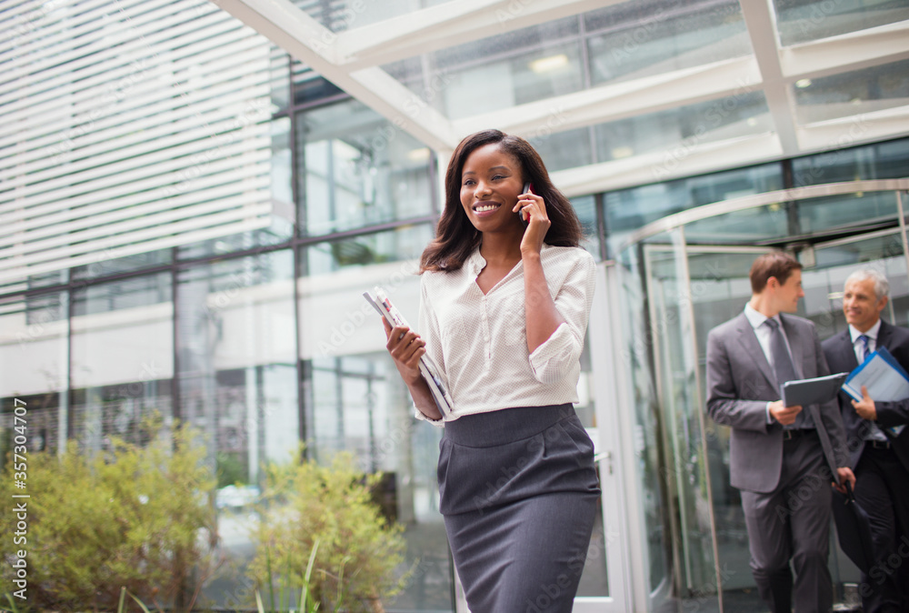 Businesswoman talking on cell phone walking out of office building Businesswoman talking on cell phone walking out of office building