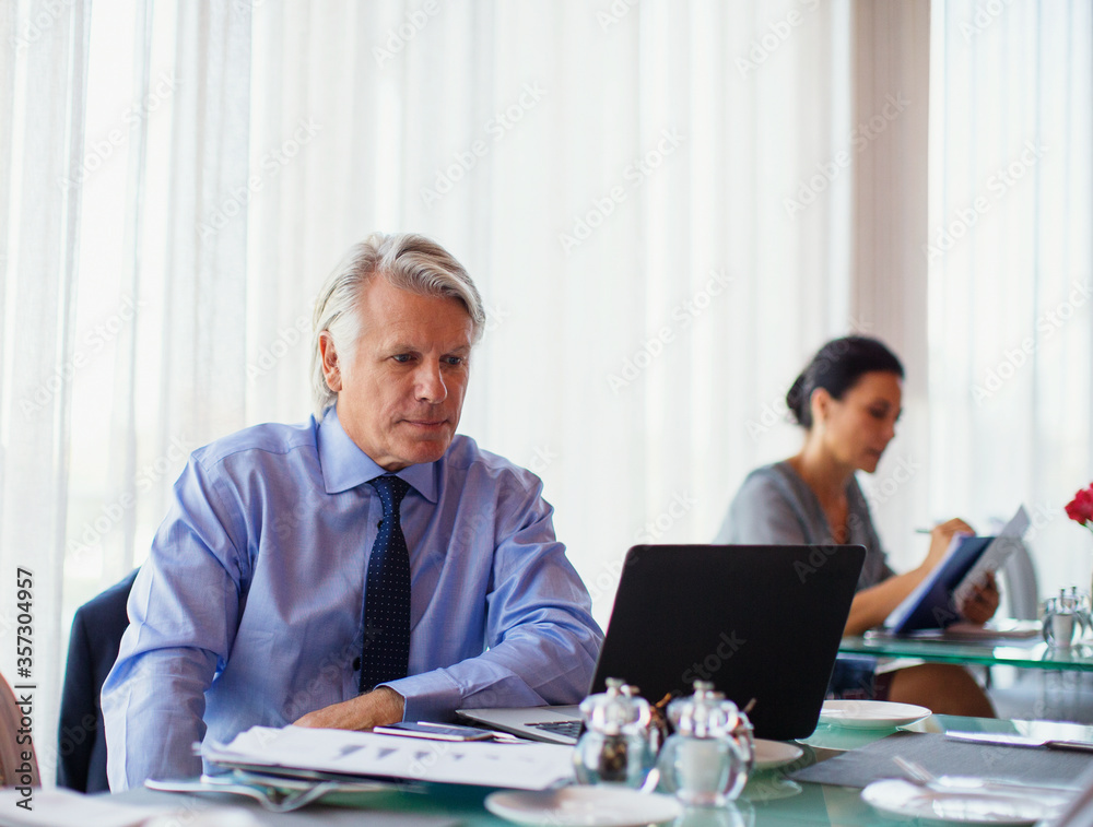 Business man using laptop in restaurant, woman in background Business man using laptop in restaurant, woman in background
