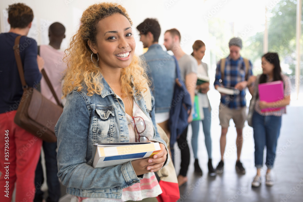 Fototapeta premium Smiling female student holding books and looking at camera