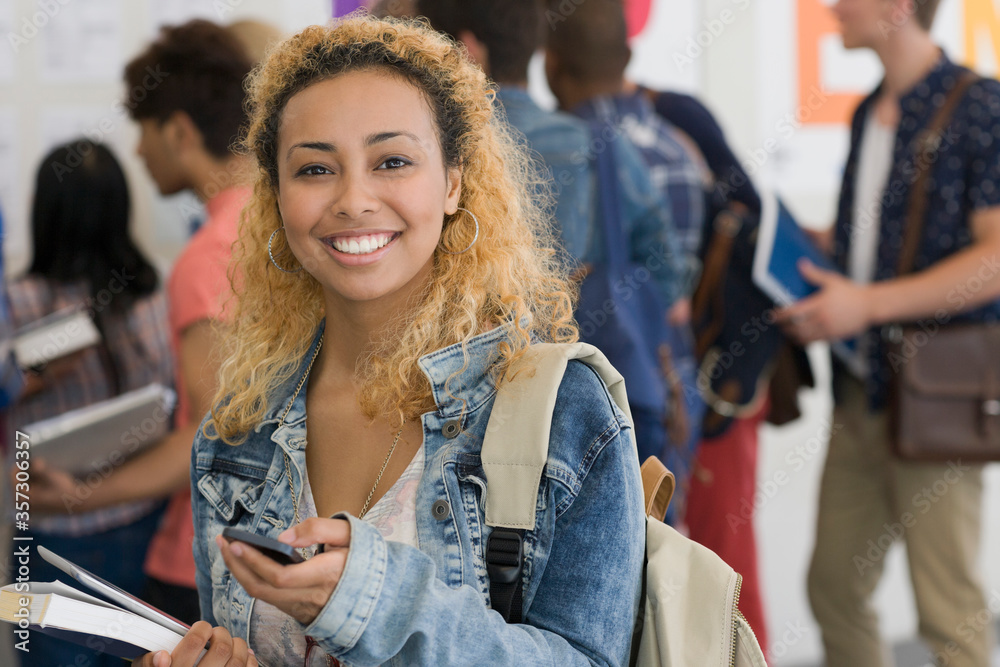 Smiling female student using cell phone with other students 