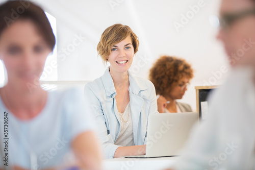 Portrait woman sitting at desk, using laptop smiling in office, colleagues 