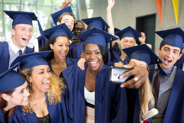 Group of smiling students in graduation gowns taking selfie on graduation day