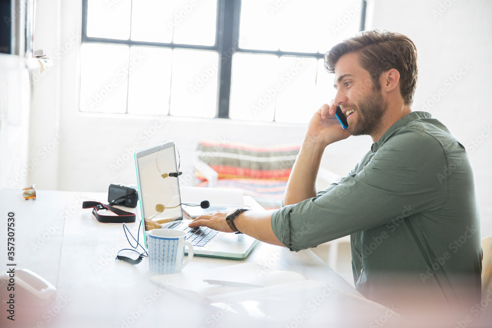 Portrait of young man sitting at desk with mobile phone and laptop Portrait of young man sitting at desk with mobile phone and laptop