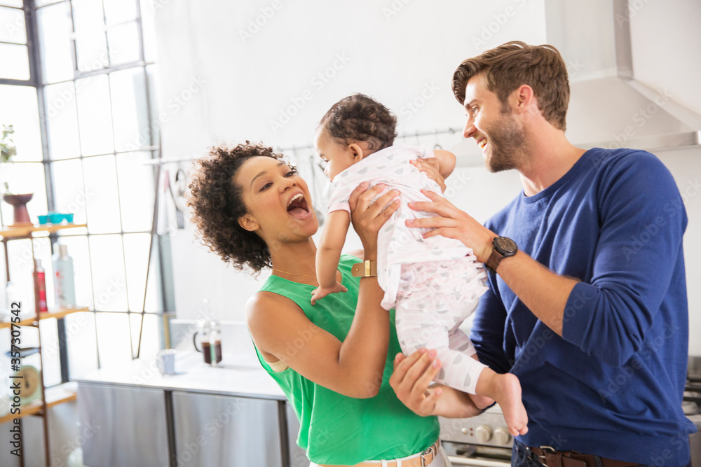 Obraz premium Happy parents holding their baby daughter in domestic kitchen