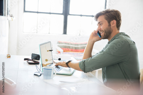 Portrait of young man sitting at desk with mobile phone and laptop