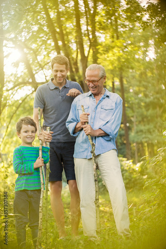 Boy, father and grandfather holding sticks in forest