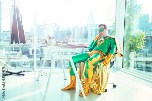 Fotografie Bored superhero slouching at desk in office