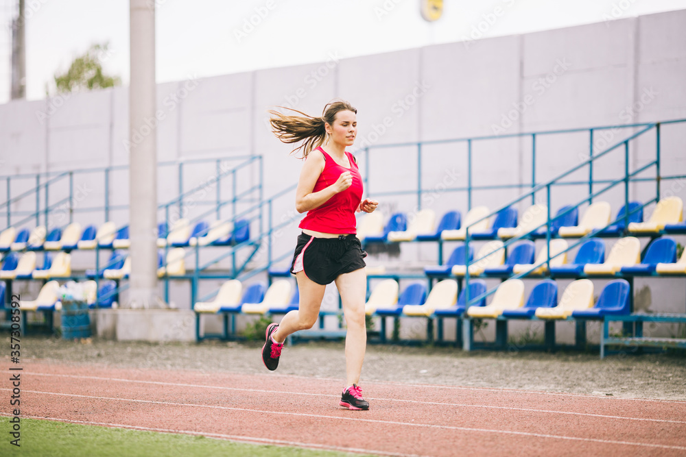 Woman Running At Stadium. Young woman running during on stadium track. Goal achievement concept. Fitness Jogging Workout on ballpark. Wellness theme. Sporty training cardio for weight loss success
