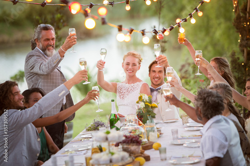 Young couple their guests toasting champagne during wedding reception in garden photo