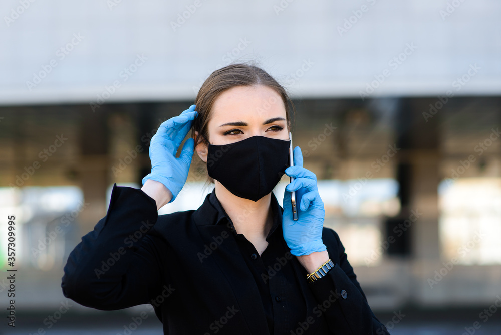 Beautiful businesswoman in a black suit in a black medical mask and gloves at the city in quarantine and isolation. Pandemic COVID-19. Selective focus