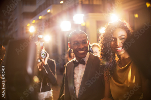 Smiling celebrity couple being photographed by paparazzi at event