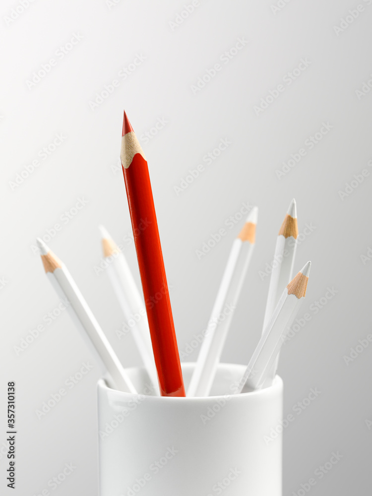 Tall red pencil in cup with smaller white pencils still life Tall red pencil in cup with smaller white pencils still life