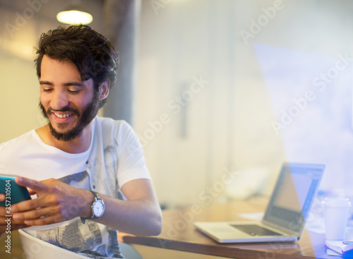 Smiling casual businessman texting with cell phone in office photo