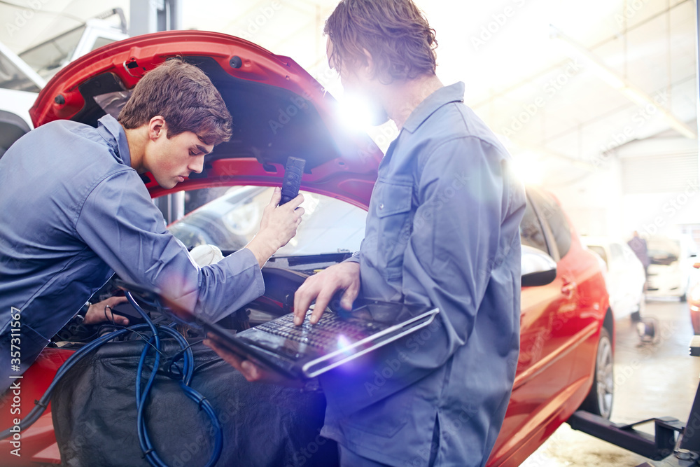 Mechanics with laptop working on car engine in auto repair shop