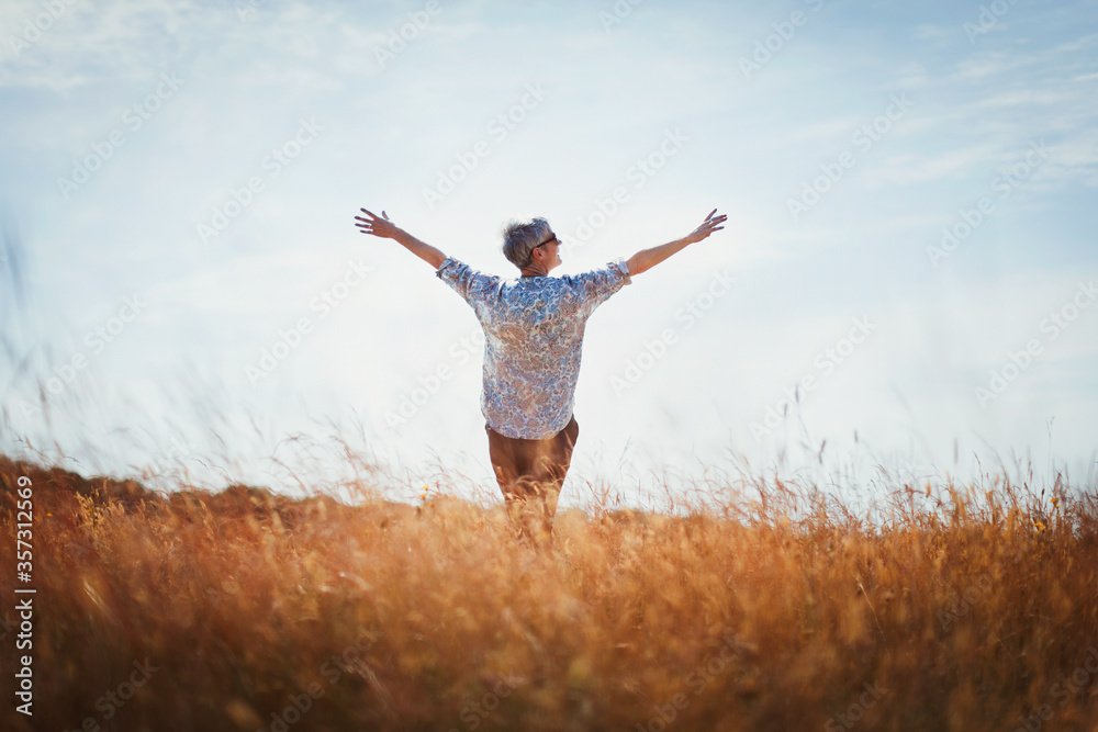 Exuberant senior woman with arms outstretched in sunny field - obrazy, fototapety, plakaty 