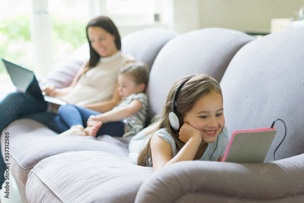 Girl with headphones and digital tablet laying on living room sofa Girl with headphones and digital tablet laying on living room sofa