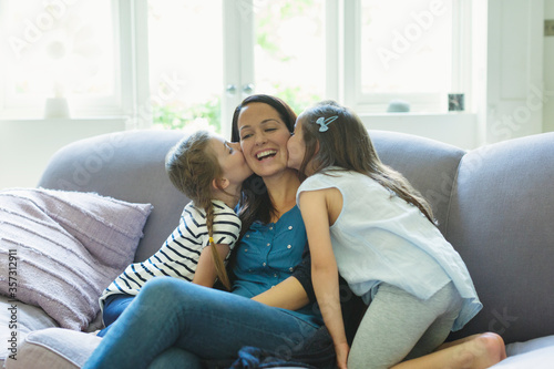 Daughters kissing mother cheeks on living room sofa