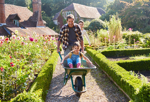 Photographie Father pushing daughter in wheelbarrow in sunny garden