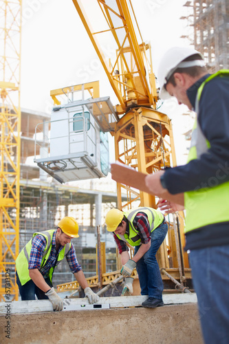 Foto Construction workers using level tool below crane at construction site