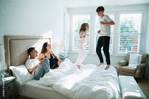 Parents watching children jumping on bed