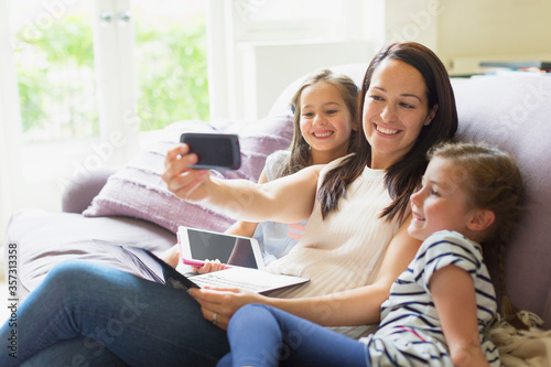 Mother and daughters taking selfie on living room sofa