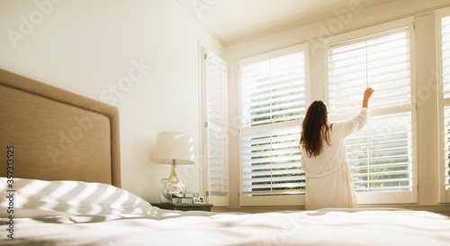 Fotografie Woman in bathrobe opening bedroom window blinds