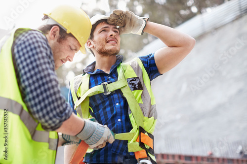 Construction worker fastening coworker‚Äôs safety harness photo