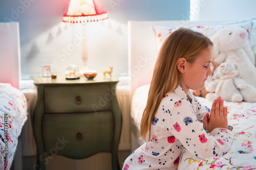 фотографія Girl in pajamas saying bedtime prayers at bed