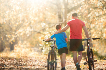 Affectionate father and son walking mountain bikes on path in woods