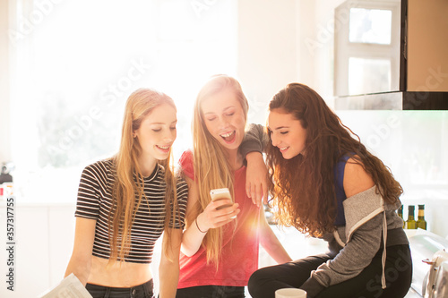 Teenage girls texting with cell phone in sunny kitchen