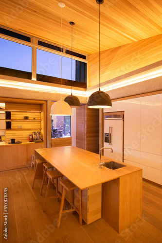 Illuminated slanted wood ceiling and pendant lights over kitchen island
