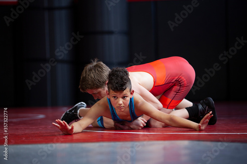 Wrestlers in red and blue singlets practicing on a red mat. 