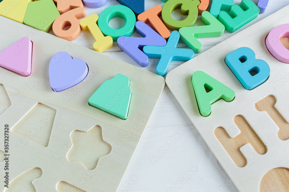 Naklejka premium Close up Multicolored wooden letters with ABC on white wooden background. Set of toys for studying alphabet. Education, back to school concept. Top view, copy space