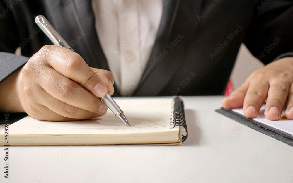Close-up of a businesswoman using a pen to write a wooden desktop notebook and a memo list. Close-up of a businesswoman using a pen to write a wooden desktop notebook and a memo list.