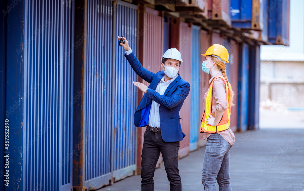 A Manager and dock worker under discussion about dock container shipping warehouse document, they wearing safety uniform hard hat ,face mask and hold radio communication. A Manager and dock worker under discussion about dock container shipping warehouse document, they wearing safety uniform hard hat ,face mask and hold radio communication.