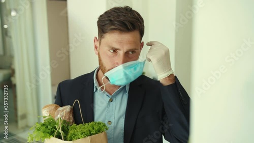 Attractive stylish man coming back home after food shopping entering house taking off mask package pandemic protection quarantine infection social distance returning virus self-care covid-19 slow