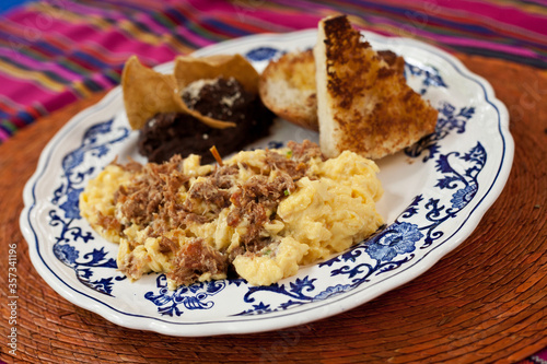 scrambled eggs with meat served with toast and tortilla chips with beans.
