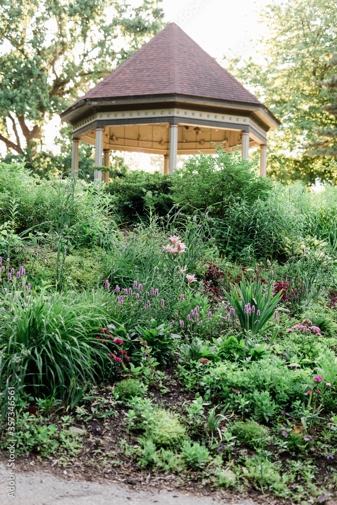 A lush garden with greenery and flowers and a gazebo in the background at a public park. A lush garden with greenery and flowers and a gazebo in the background at a public park.