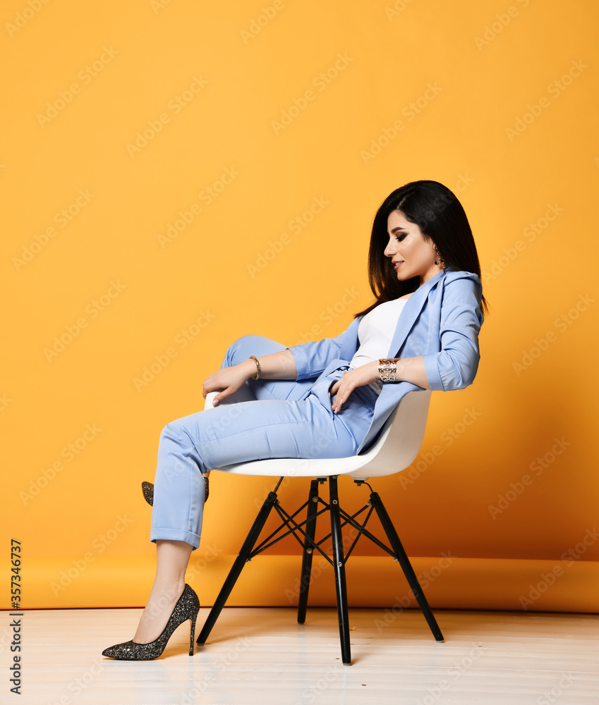 Stylish business woman brunette in blue official suit and high-heeled shoes sitting in designer armchair looking down Stylish business woman brunette in blue official suit and high-heeled shoes sitting in designer armchair looking down