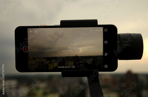 Savar, Dhaka, Bangladesh-June 5, 2020:  Mobile phone Google pixel 3A is shooting a video using gimbal dramatic sky with clouds background is bokeh in the afternoon after raining Video filming concept. photo