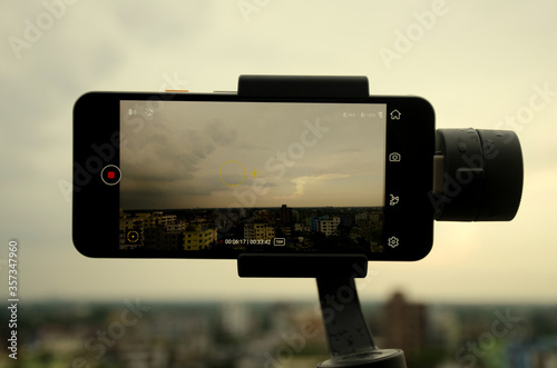 Savar, Dhaka, Bangladesh-June 5, 2020:  Mobile phone Google pixel 3A is shooting a video using gimbal dramatic sky with clouds background is bokeh in the afternoon after raining Video filming concept. photo