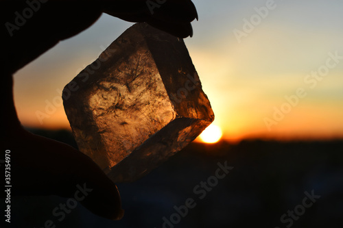 A close up image of transparent champagne calcite held against a glowing orange sunset. 