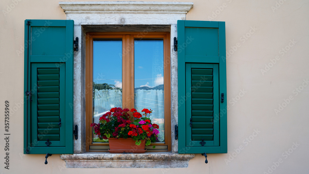 Fototapeta premium A blank pastel wall of a residential building window with shutters and flower pot in Italy with copy space.