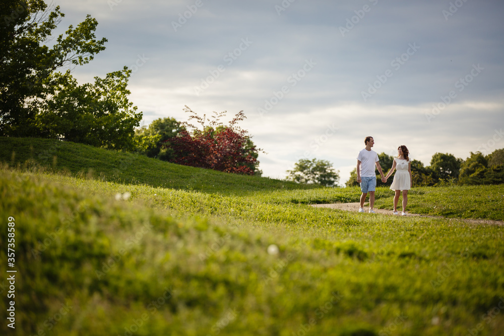 Young man and woman couple walk in the meadow. Tender holding each other. Spring lovestory. Brown-haired girl with curled hairs and man weared in casual and denim. Young family