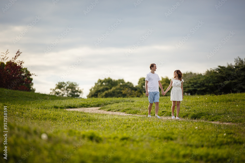 Young man and woman couple walk in the meadow. Tender holding each other. Spring lovestory. Brown-haired girl with curled hairs and man weared in casual and denim. Young family