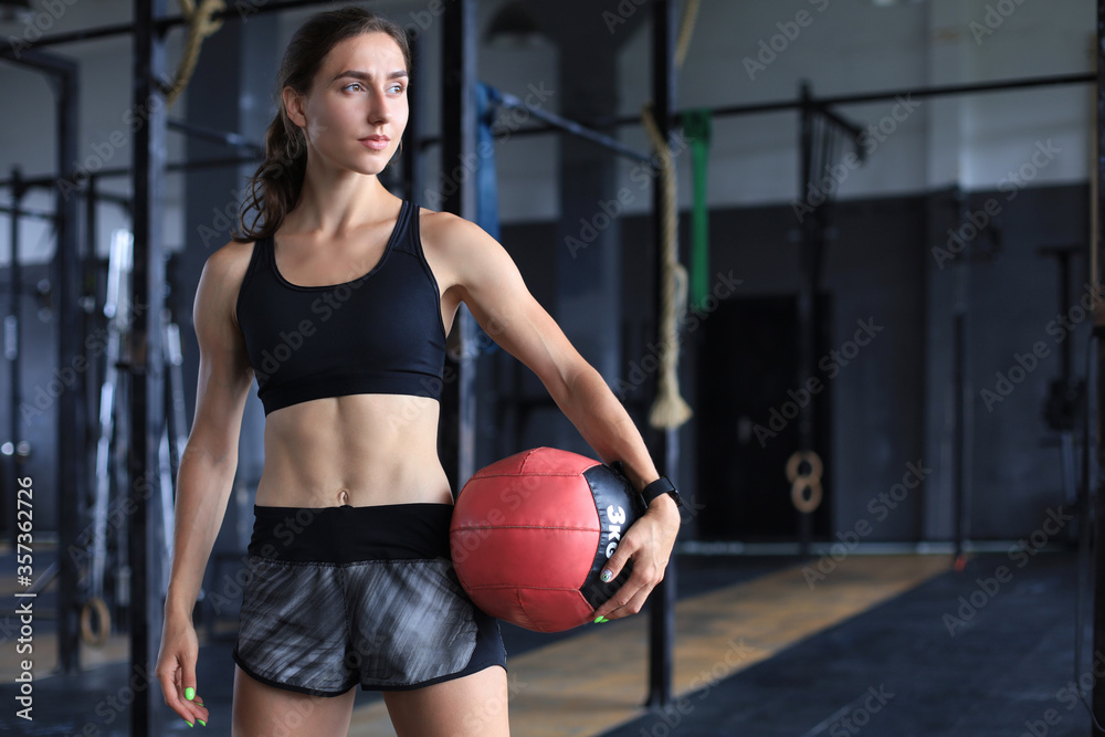 Muscular strong woman carrying medicine ball at crossfit gym.