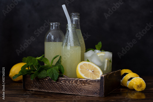 bottles of cold lemonade, fresh lemons and mint in wooden box