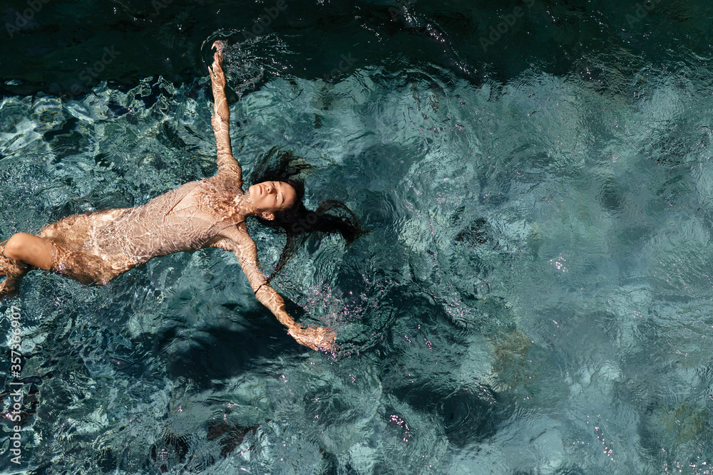 Attractive young woman floating in a swimming pool with her arms ...