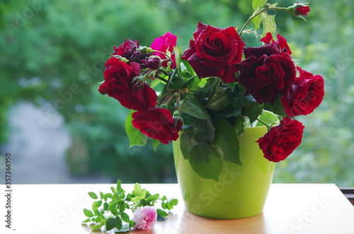 Fototapeta Naklejka Na Ścianę i Meble -  A bouquet of red roses in a green vase standing on a windowsill.