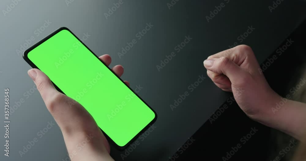 Young woman sitting on a chair near window and using smartphone with green screen Young woman sitting on a chair near window and using smartphone with green screen